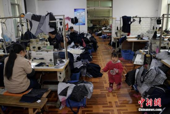 资料图：成都郫都区安靖镇土地村某服装加工厂车间内一小女孩正在玩耍，其母亲正坐在缝纫机前赶制服装。